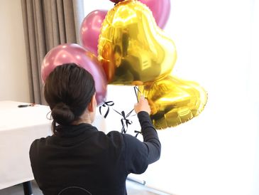 Person holding gold heart-shaped and pink balloons.