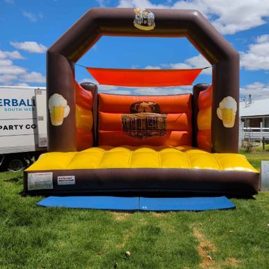 Inflatable bounce house with beer mug designs outdoors.