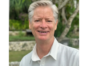 Smiling older man with gray hair outdoors in casual white shirt.