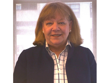 Smiling woman with shoulder-length hair in a checked shirt and dark jacket.