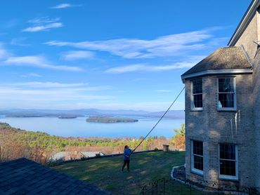 Person flying a kite near a large house with a scenic lake and island view.