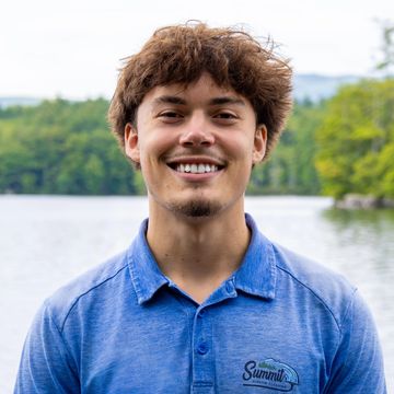 Young man smiling outdoors near a lake.