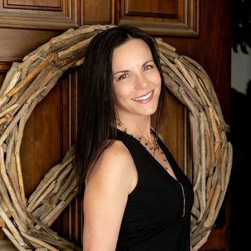 Jennifer Hall, intuitive counselor and life coach, smiling warmly in a doorway framed by a natural g