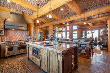 Rustic kitchen with wooden beams, brick walls, and a large island.