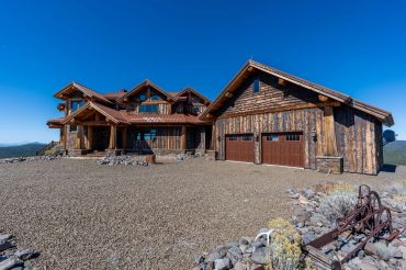 Large rustic wooden house with a three-car garage under a clear blue sky.