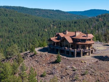 Large rustic house on a rocky hill surrounded by dense forest.