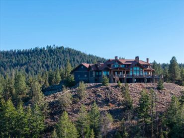 Large house perched on a forested hill under a clear blue sky.