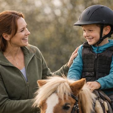 A smiling woman and child with helmet, the child riding a pony.