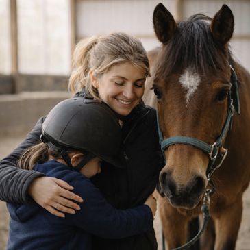 A woman and child hugging next to a horse in a stable.