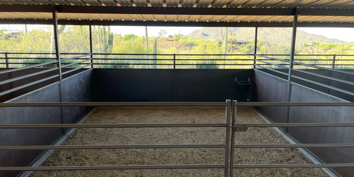 Empty horse stall with metal bars and desert landscape view.