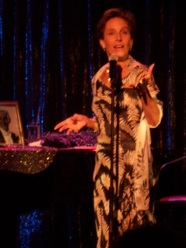 Woman singing on stage with a microphone in a patterned dress.