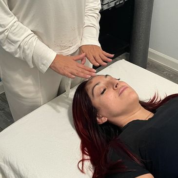 A woman receiving a relaxing Reiki treatment on her forehead.