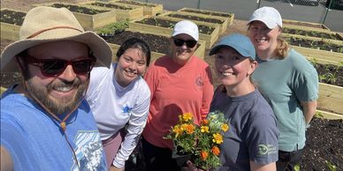 A group of five smiling people in a garden with raised beds and flowers.