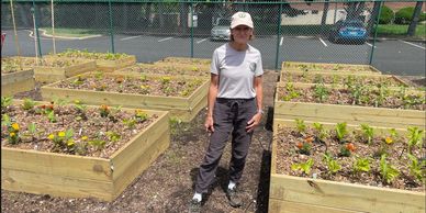 Person standing in a garden with multiple raised wooden planter boxes.