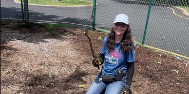A woman gardening outdoors, holding a tool and smiling.
