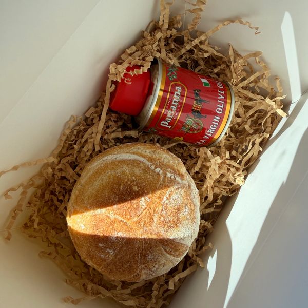 A rustic bread loaf and a can of extra virgin olive oil in a box.