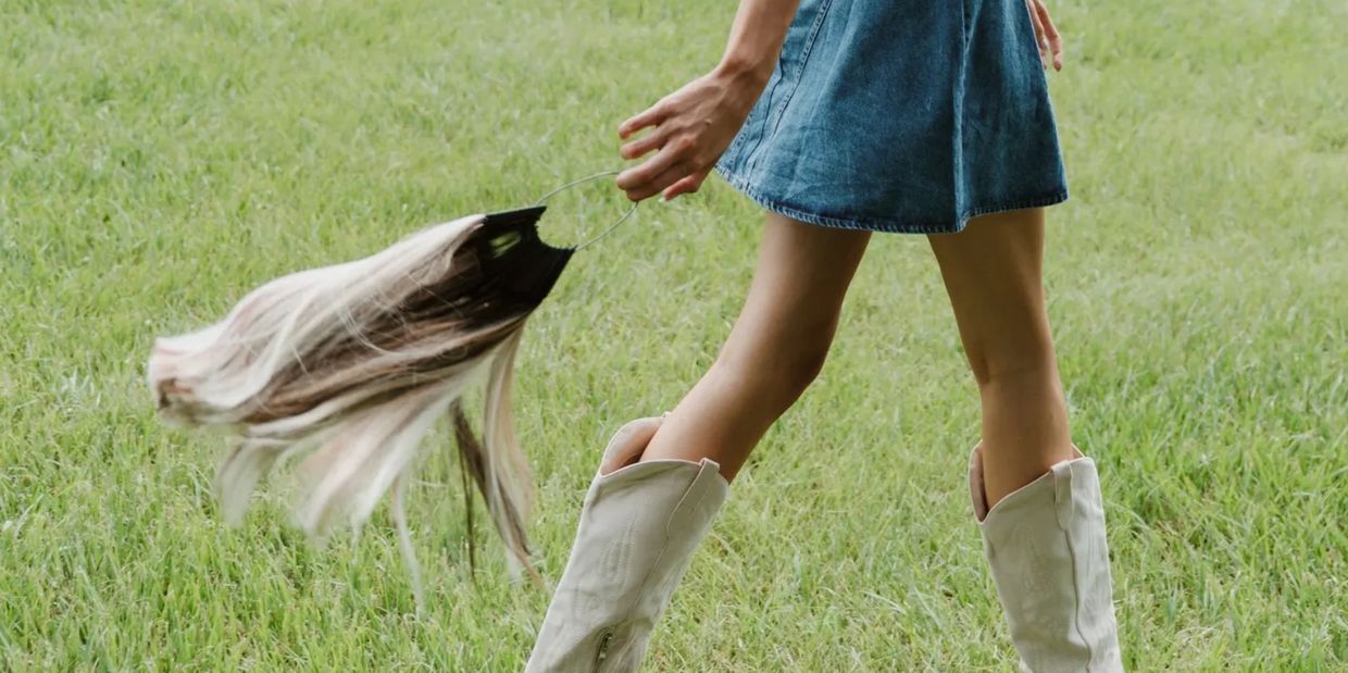 Person in denim skirt and boots holding a hairpiece outdoors.