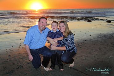 Family portrait with a vivid sunset on the beach. Mom and Dad with their young son hugging.