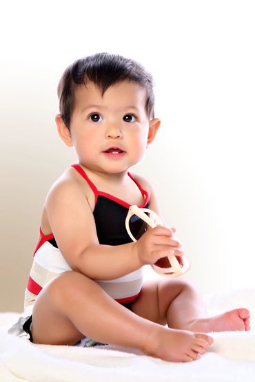 Toddler wearing swimsuit holding sunnies in studio with white backdrop