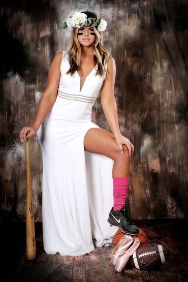Studio portrait of a HS Senior in white dress with baseball bat and cleats