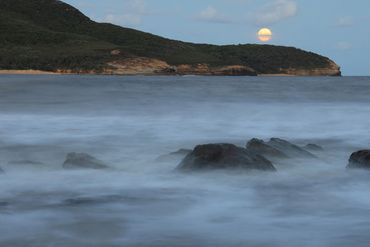 photo of the sea in a bay with headland and moon