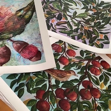 picture of several artworks of birds, fruit and flowers lying on a table