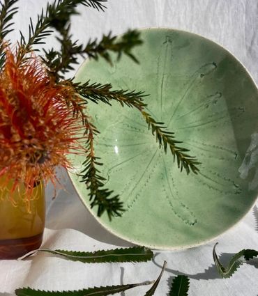 Green ceramic bowl with leaf imprint and orange-red flowers.