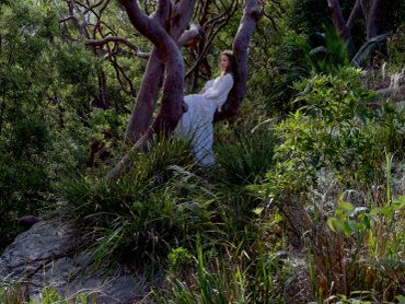 Woman in white dress sitting on tree branch in forest.