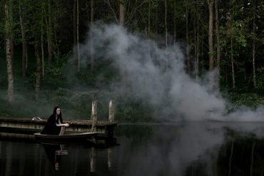 A woman in black on a boat in a foggy forest lake.