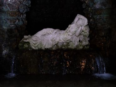 White reclining statue in a dark cave with water flowing.