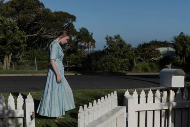 Woman in blue dress walking near a white fence.