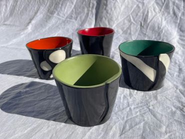 four ceramic mugs that are black and white outside with bright colours inside