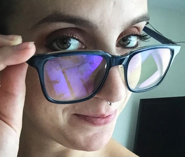 Color photo of a caucasian gender fluid human’s face, wearing glasses, pulling them below the eyes.