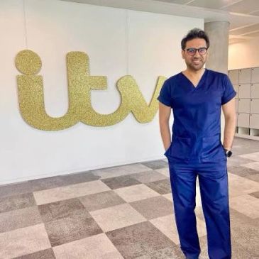 Man in blue scrubs standing by an ITV sign.