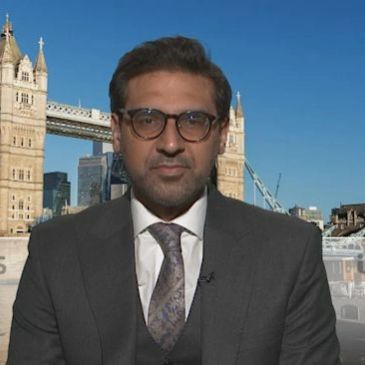 Man in suit and glasses with Tower Bridge background.