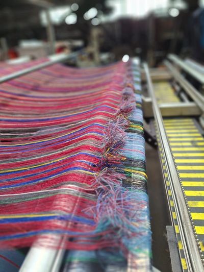 Colorful striped fabric being woven on a loom in a textile workshop.
