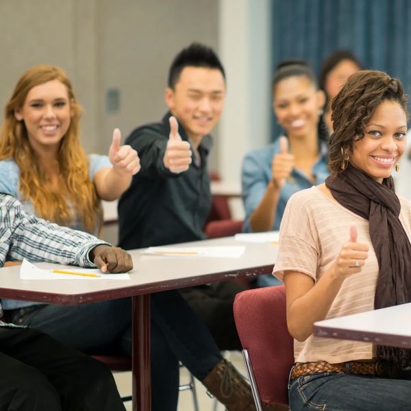 Students in a classroom giving thumbs up and smiling.