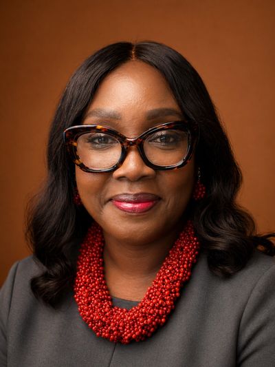 Smiling woman with tortoiseshell glasses and red beaded necklace.