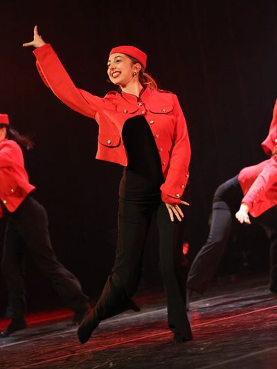 Danseuse souriante en costume rouge et noir sur scène.