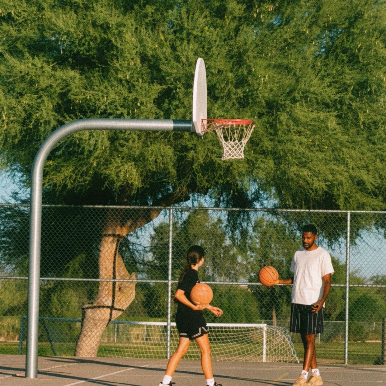 Two people playing basketball outdoors.