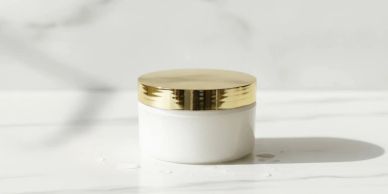 White cosmetic jar with gold lid on marble surface.