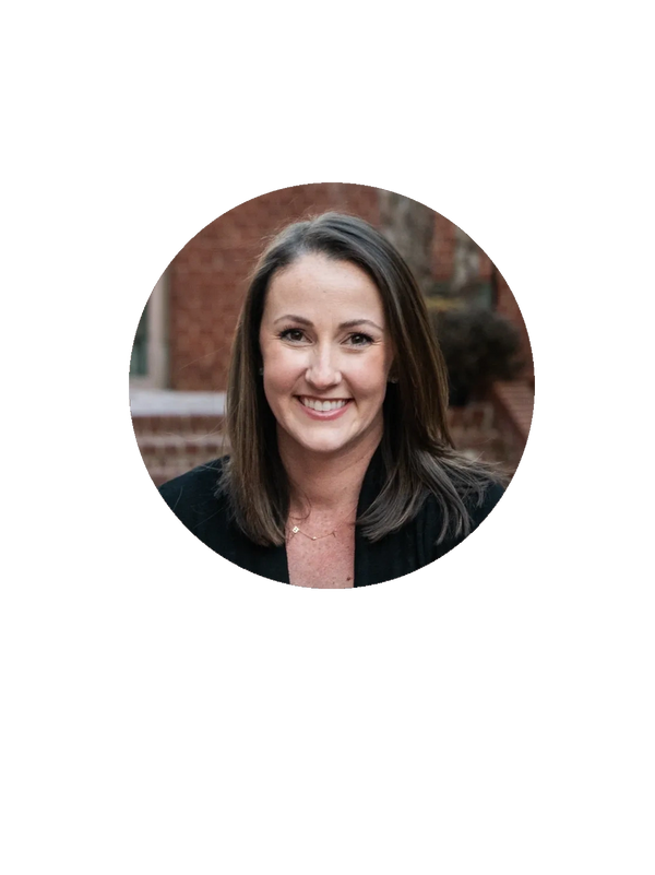 Smiling woman with straight brown hair and a black top, outdoors against a brick background.