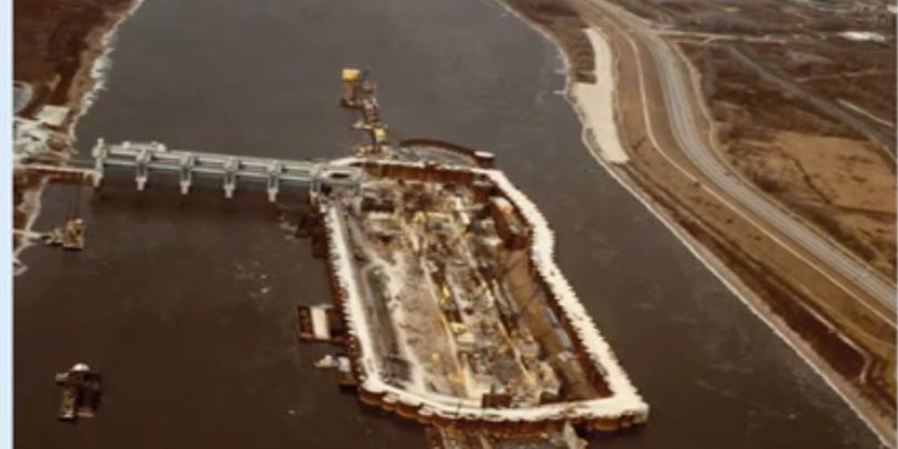 Aerial view of a dam construction site on a river with adjacent highway.