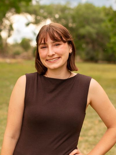 Young woman smiling outdoors with hand on hip.