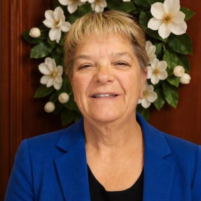 Smiling woman in blue blazer with floral background.
