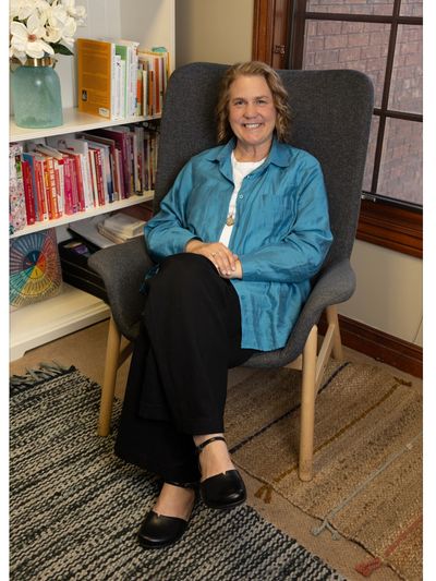 Smiling woman seated comfortably in a cozy room with books and flowers.