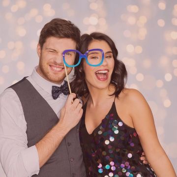 Couple embracing while smiling and holding faux glasses.