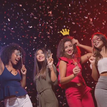 Group of four women posing with champagne and props with confetti falling behind them.