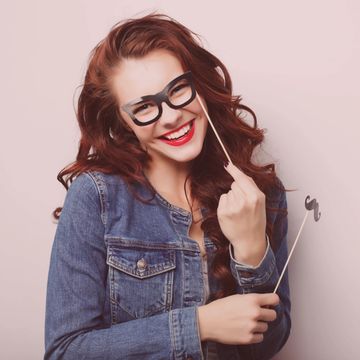 Woman posing and smiling holding up faux glasses