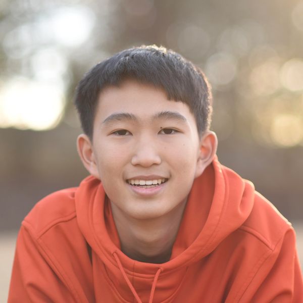 Young man smiling in an orange hoodie outdoors.